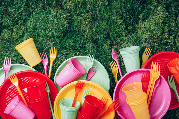 Colored plastic disposable tableware on green grass moss background. Top view. Copy space. Birthday